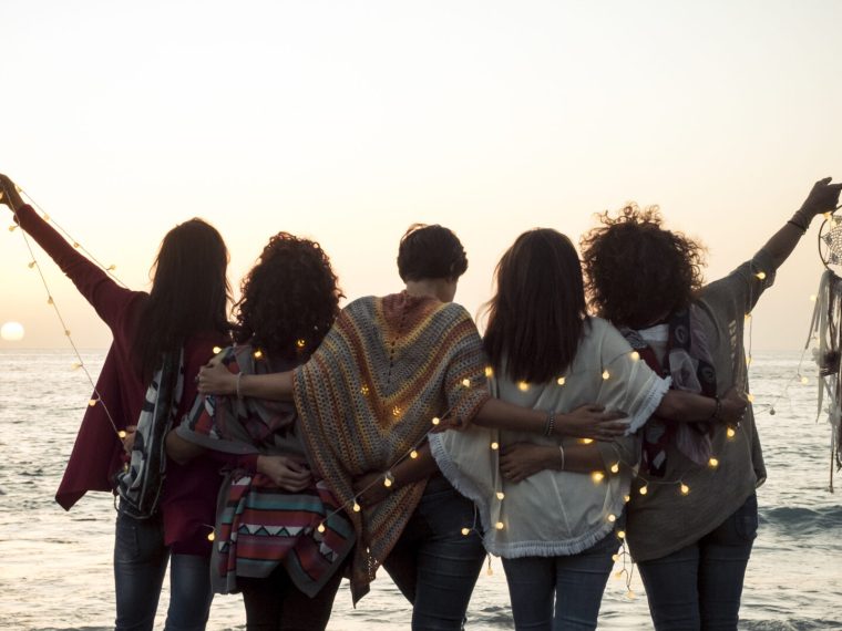 Romance and emotion concept with group of people women friends viewed from back hugging and ejoying the sunset in outdoor nature sea vacation concept - friendship and freedom for travelers